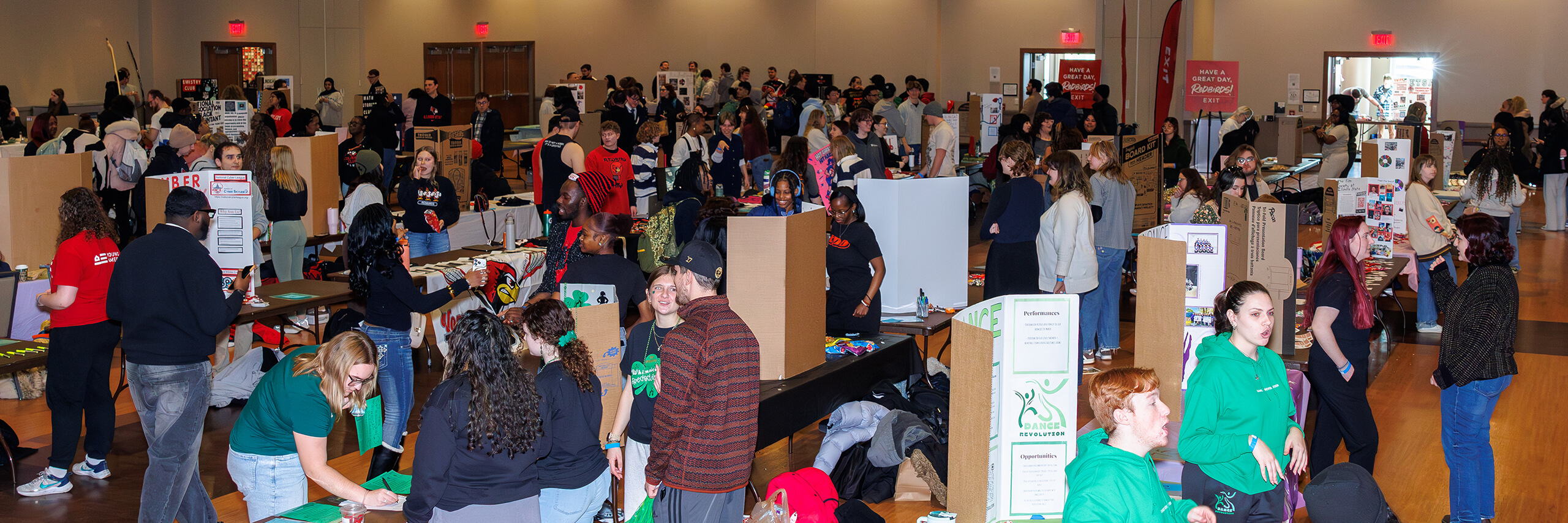 a crowded indoor student organization fair with numerous booths, displays, and attendees.